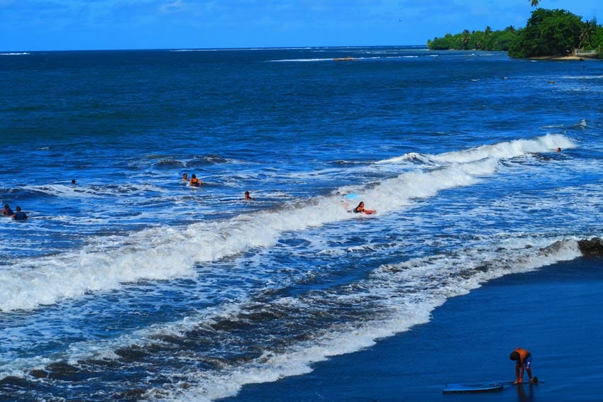children surfing in Tahiti Iti black sand beach French Polynesia